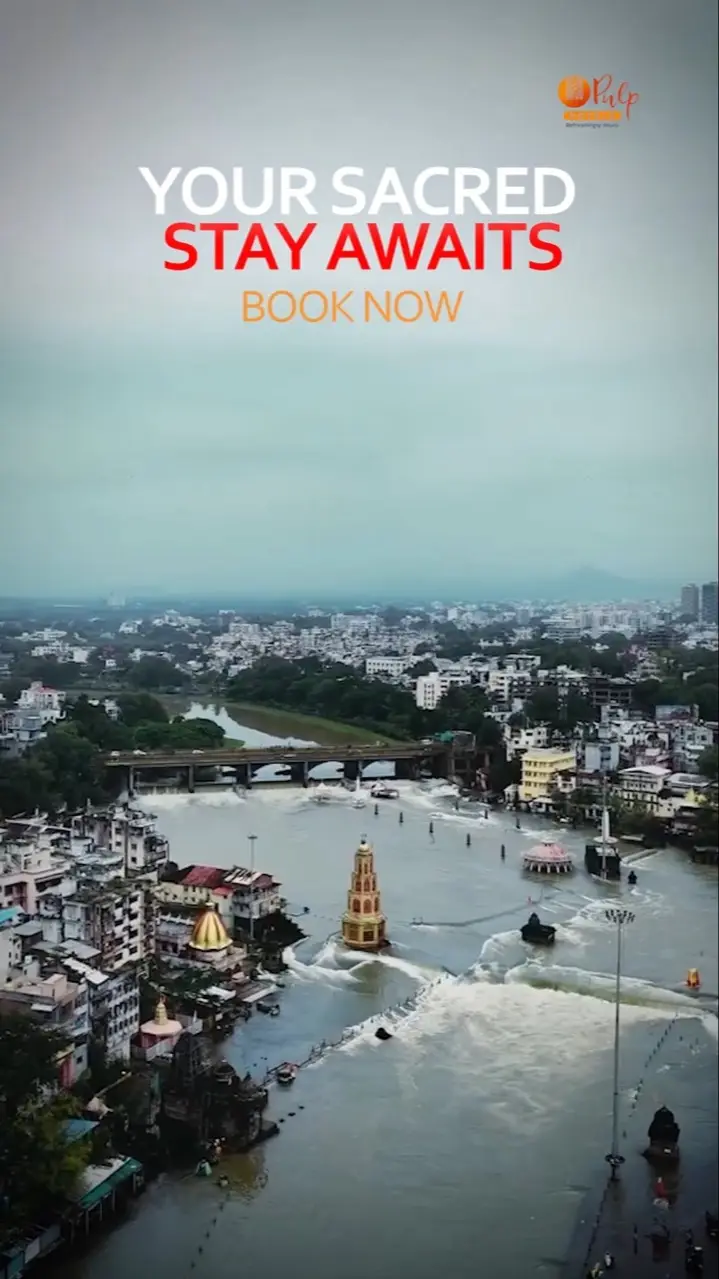 Aerial view of a river town's ghats and temples in flowing water, with the words Your Sacred Stay Awaits — Book Now